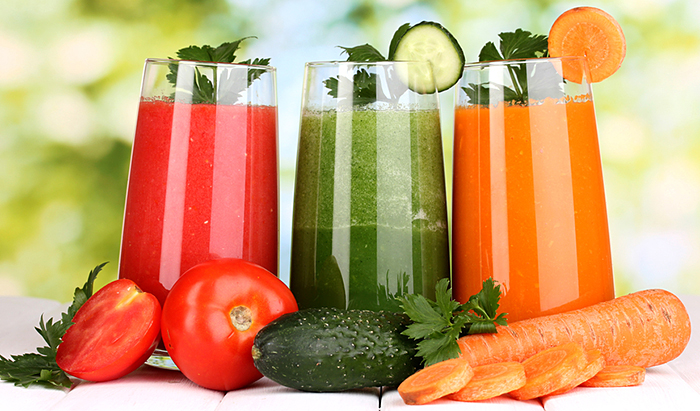 Fresh vegetable juices on wooden table, on green background